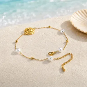 Detail shot of golden shell charm and pearl anklet on sand background, beach jewelry style.