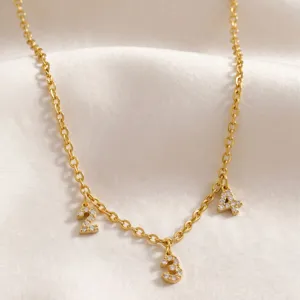 Primer plano detallado del collar con dije de número bañado en oro con circonitas brillantes.