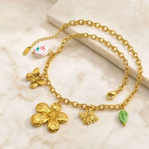 Primer plano detallado del collar de dijes dorados con colgantes florales, de abeja y mariposa.
