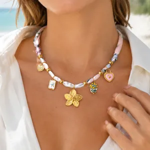 Gros plan de collier avec ruban de soie rose, perles dorées et charmants pendentifs floraux.