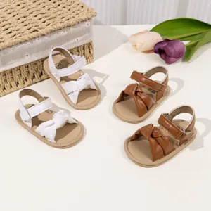 Close-up detail of infant baby sandals showing soft bow knot design and adjustable strap.