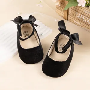 Detailed shot of black velvet baby princess shoes with cute bow and soft soles for infants.