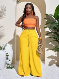 Detail view of high waist wide leg pants in yellow with matching orange crop top, beach style.
