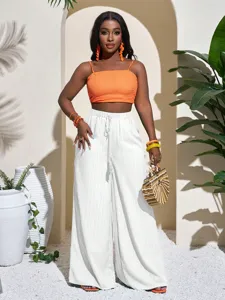 Stylish women's orange crop top and white high waist wide leg pants set for casual beach wear.