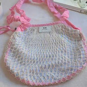 Detail view of the pink and blue gingham mesh shoulder bag with ruffle strap and handmade label.