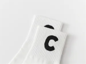 Close-up detail of white cotton mid-tube socks featuring a bold black letter C graphic design.
