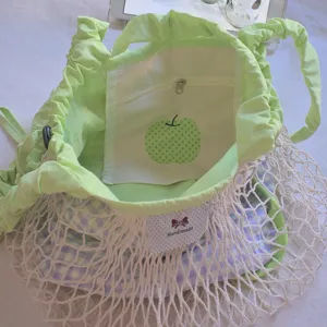 Close-up of light green nylon drawstring bag with apple print inner pocket and mesh layer.