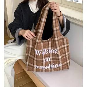 Detail shot of a brown plaid woolen tote bag featuring white 3D embroidery lettering.