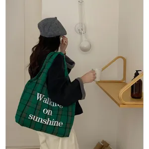 Close-up detail of green plaid woolen tote bag featuring 3D embroidered text and daily scene.