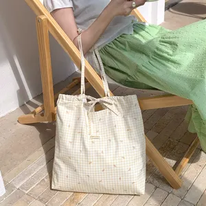 Dettaglio ravvicinato della borsa shopper in tela a quadretti gialli con fiocchi e coulisse.