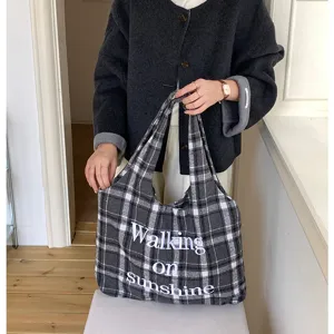 Detail view of a black and white plaid wool tote bag featuring white embroidered text.