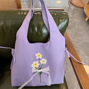 Detailopname van de zoete paarse schoudertas met mooie bloemenborduurwerk en witte kanten strik.