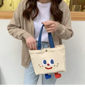 Sac cabas de déjeuner en toile mignon avec visage brodé et petits pieds rigolos.