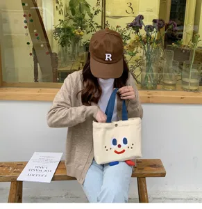 Vue détaillée du sac à lunch en toile mignon avec visage amusant et poignées bleues.