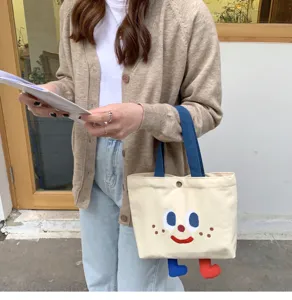 Sac à lunch bento en toile mignon avec visage brodé et détails de pieds suspendus.