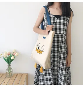Canvas tote bag detail showing cartoon duck graphic design, carried by model in casual dress.