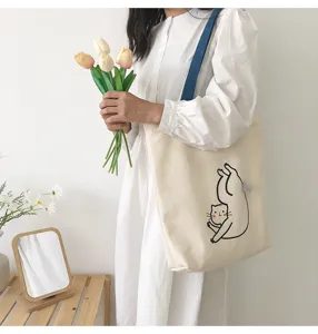 Detailed view of a cream canvas tote bag with a cute cat print and blue shoulder strap.