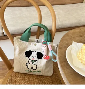 Detailed shot of the cute corduroy handbag featuring embroidered puppy and green handles.