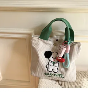 Corduroy handbag detail showing cute puppy embroidery and green handles, soft fabric.