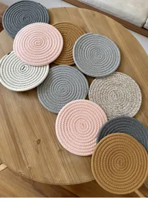 Detailed shot of round woven cotton coasters in assorted colors on a rustic wooden table.