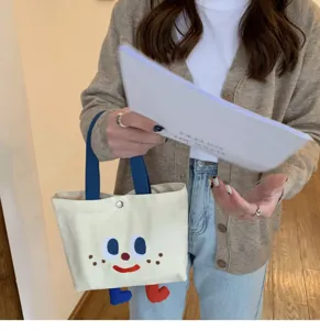 Joli sac cabas en toile avec visage mignon et jambes pendantes pour école et déjeuner.