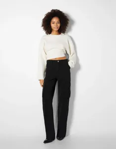Detailansicht des lässigen Damen-Outfits mit weißem Pullover und schwarzer Cargohose.