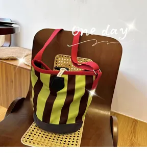 Detailansicht einer retro gestreiften Eimertasche mit roten Gurten auf Holzstuhl.