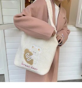 Close-up detail of fluffy white plush shoulder bag with cute bear embroidery and strap.