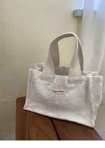 Detail shot of a white floral textured canvas mini handbag showcasing the delicate fabric and branded patch.