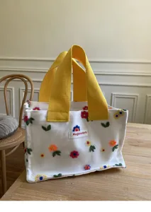 Detailed view of mini white canvas tote bag with colorful floral embroidery and yellow handles.
