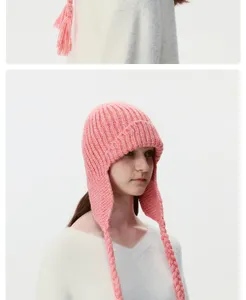 Pink knitted earflap hat detail view, cozy winter trapper hat with stylish braid tassels.