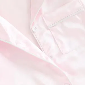 Gros plan détaillé d'une chemise de pyjama en satin rose avec un passepoil blanc.