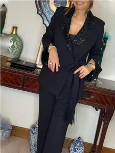 Black two-piece suit detail showing sequin lapel, long sleeves and tassel belt in room.