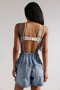 Back view detail of casual light wash denim overalls shorts paired with white lace bralette.