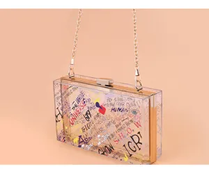 Transparent acrylic box handbag featuring colorful graffiti print and gold chain strap detail.