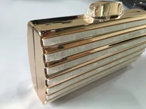 Gold metal frame evening clutch with white acrylic stripes, elegant detail shot for women.