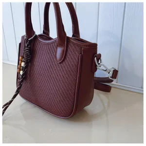 Nahaufnahme der braunen Handtasche mit geflochtener Textur, Holzperlenanhänger und Metallbeschlag.
