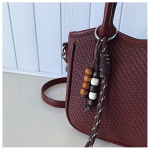 Detailansicht der braunen gewebten Umhängetasche mit Holzperlen und Metallring-Accessoire.