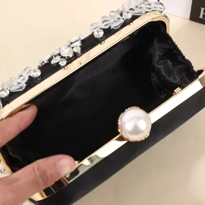 Pochette de soirée noire en satin avec strass, bordure dorée et fermoir perle.