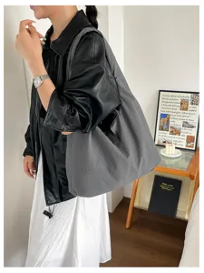 Detailed view of a casual large grey shoulder bag worn by a model in a stylish room setup.