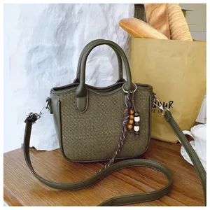 Detailansicht der olivgrünen gewebten Umhängebag mit Ledergriff und Holzkugelanhänger.