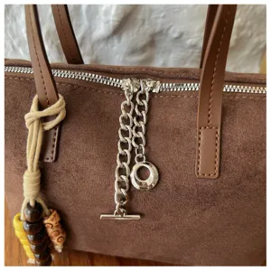Nahaufnahme einer stilvollen braunen Wildleder Handtasche mit Silberkette und T-Steg Anhänger.