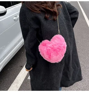 Pink heart-shaped plush cross-body bag detail showing soft furry texture and gold chain strap.