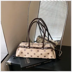 Detailed view of stylish beige polka dot shoulder bag with brown straps on book prop.