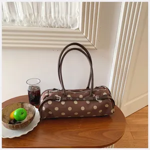 Brown polka dot shoulder bag detail showcasing cylindrical design, dual straps and metallic buckle.