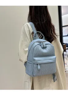 Close-up detail of light blue quilted backpack with front zip pocket and sturdy straps.