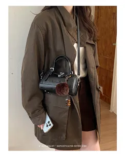 Gros plan détaillé du sac Boston en cuir noir avec pompon et tenue chic quotidienne.