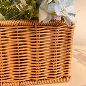 Close-up detail of imitation rattan woven storage basket with artificial floral arrangement.