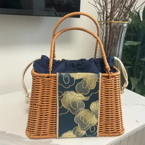 Detailed view of a trapezoid woven handbag with blue drawstring lining and gold cloud embroidery.