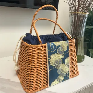 Trapezoid imitation rattan woven handbag featuring chic blue cloud embroidered panel and drawstring.